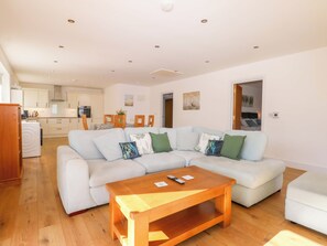 A modern living room with a sectional sofa, a wooden coffee table, and a kitchen in the background. - Bluebell Cottage (Maidstone)