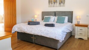 A bedroom with a bed, two bedside tables, a wooden door, and a painting on the wall. - Bluebell Cottage (Maidstone)