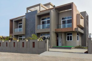 A modern multi-story residential building with a flat roof, large windows, and a balcony.