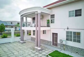 Ein zweistöckiges Haus mit einer überdachten Terrasse, einem gepflasterten Innenhof und einer kleinen Rasenfläche.