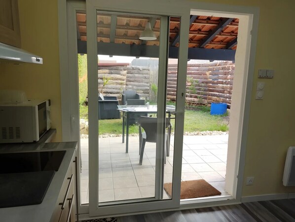 A kitchen with a microwave, a sliding glass door leading to an outdoor patio with a table and chairs, and a wooden fence in the background. - Studio "Les Dunes" with Shared Pool, Les Cigales du Bassin in Gujan-Mestras (Gujan-Mestras)