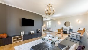 A modern living room with a flat-screen TV, a glass coffee table, a sofa, and a chandelier.