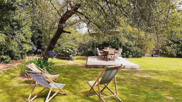 A patio area with a table and chairs, surrounded by lush greenery and trees. - COTTAGE CLOSE TO THE SEA. Pets allowed, ideal for families (lezardrieux)