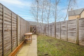 Ein umzäunter Garten mit Holztisch und Stühlen, einer Rasenfläche und kahlen Bäumen.