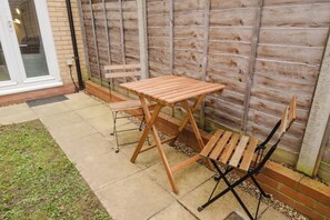 A patio with a wooden table and chairs, a brick wall, and a door. - Spacious 4 Bed House With 3 Bathrooms & Parking (Bedford)