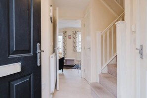Ein Gang mit einer schwarzen Tür, weißen Wänden und einer Treppe, die in einen anderen Raum führt.