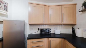 A kitchen with wooden cabinets, a black countertop, a stainless steel refrigerator, a microwave, and a toaster. - Spacious 4 Bed House With 3 Bathrooms & Parking (Bedford)