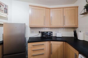 Una cocina con armarios de madera, encimera negra, refrigerador de acero inoxidable, microondas y tostadora.