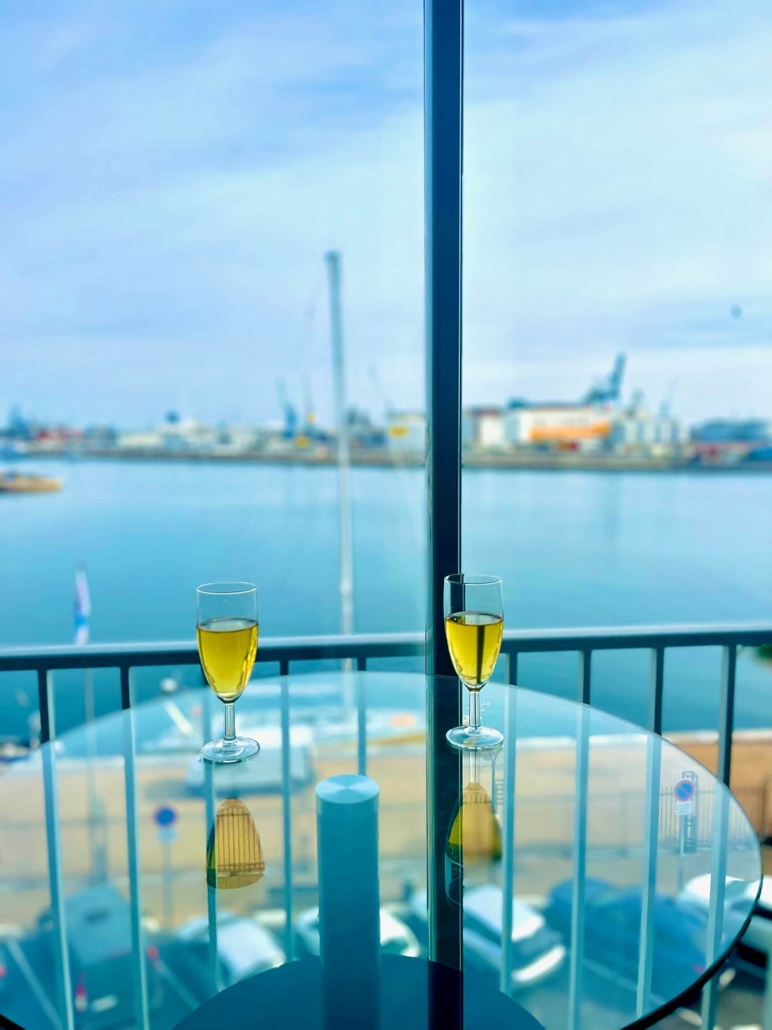 A table with two glasses of wine and a view of a harbor.
