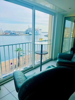 Un balcon donnant sur une marina, une table avec des verres et un canapé vert.