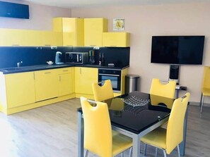 Una cocina moderna con armarios amarillos, encimera negra y un comedor con sillas amarillas y una mesa de vidrio.