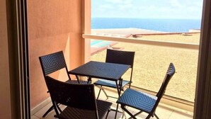 A balcony with a view of the beach, a table, and two chairs.