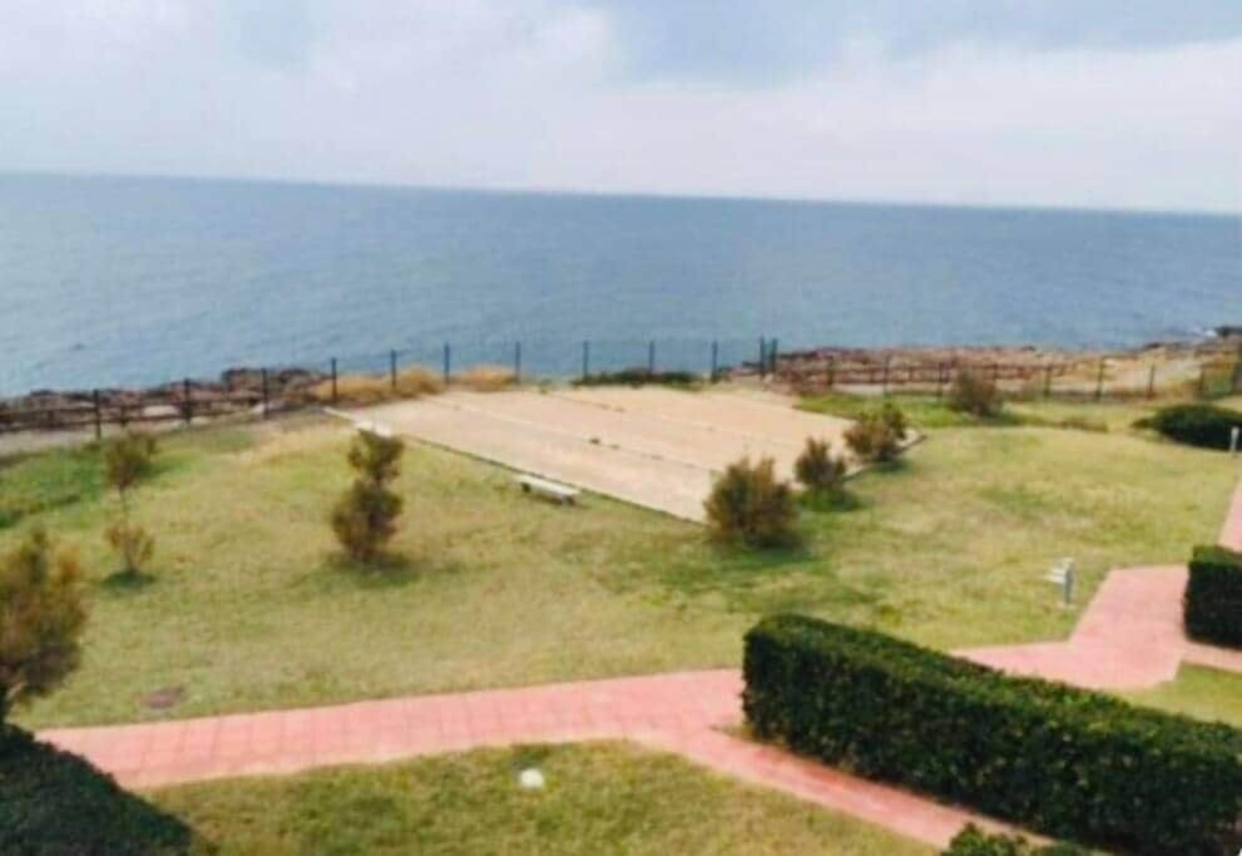Une vue sur la côte, avec une zone pavée, une clôture et un sentier menant à la mer.