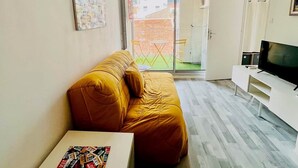 A small, cozy room with a sofa, a TV, and a table. There's a sliding door leading to an outdoor area. - "Ophélia 22" Nice T2 with air conditioning and parking (Sète)