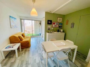 A compact living space with a sofa, a dining table, a kitchenette, and a sliding glass door leading to a balcony. - "Ophélia 22" Nice T2 with air conditioning and parking (Sète)