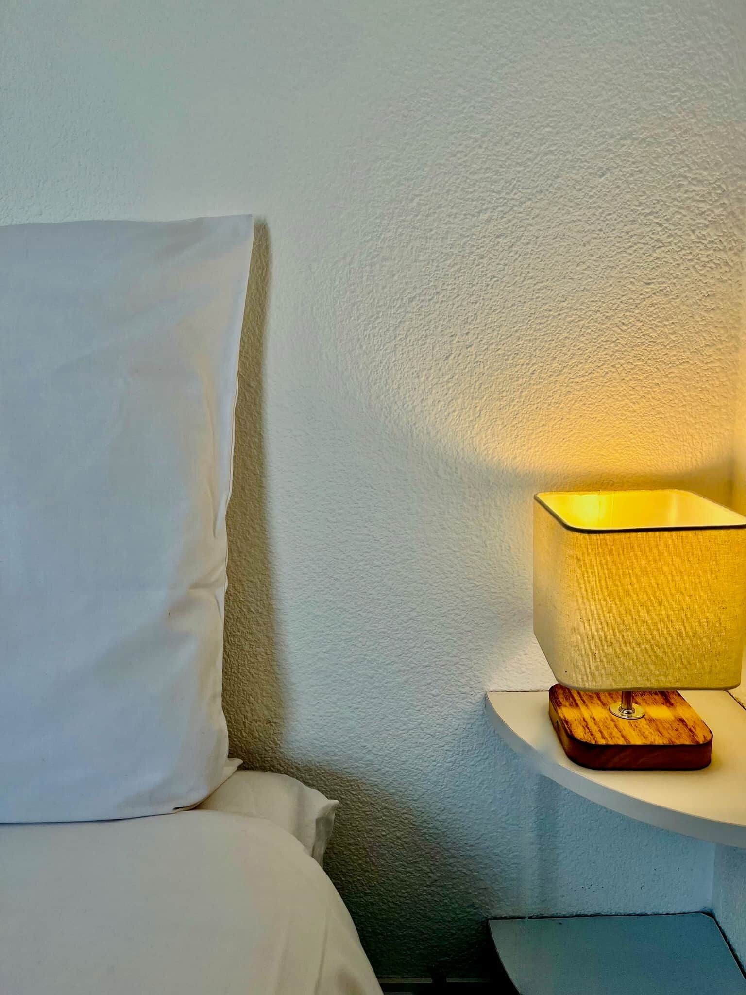 Een bed met witte beddengoed, een nachtkastje met een lamp, en een structuurwand.