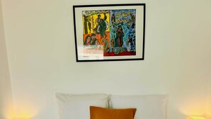 A hotel room with a neatly made bed, a single orange pillow, two bedside lamps, and a framed artwork above the bed. - "Ophélia 22" Nice T2 with air conditioning and parking (Sète)