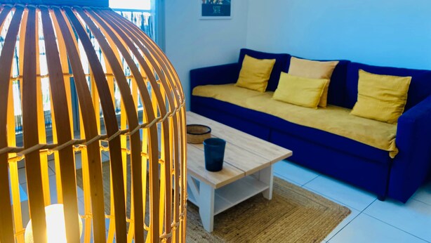 A room with a blue sofa, yellow cushions, a wooden coffee table, and a hanging light fixture. - ''Loulou'' T2 modern, bright in the city center, wif parking (Sète)