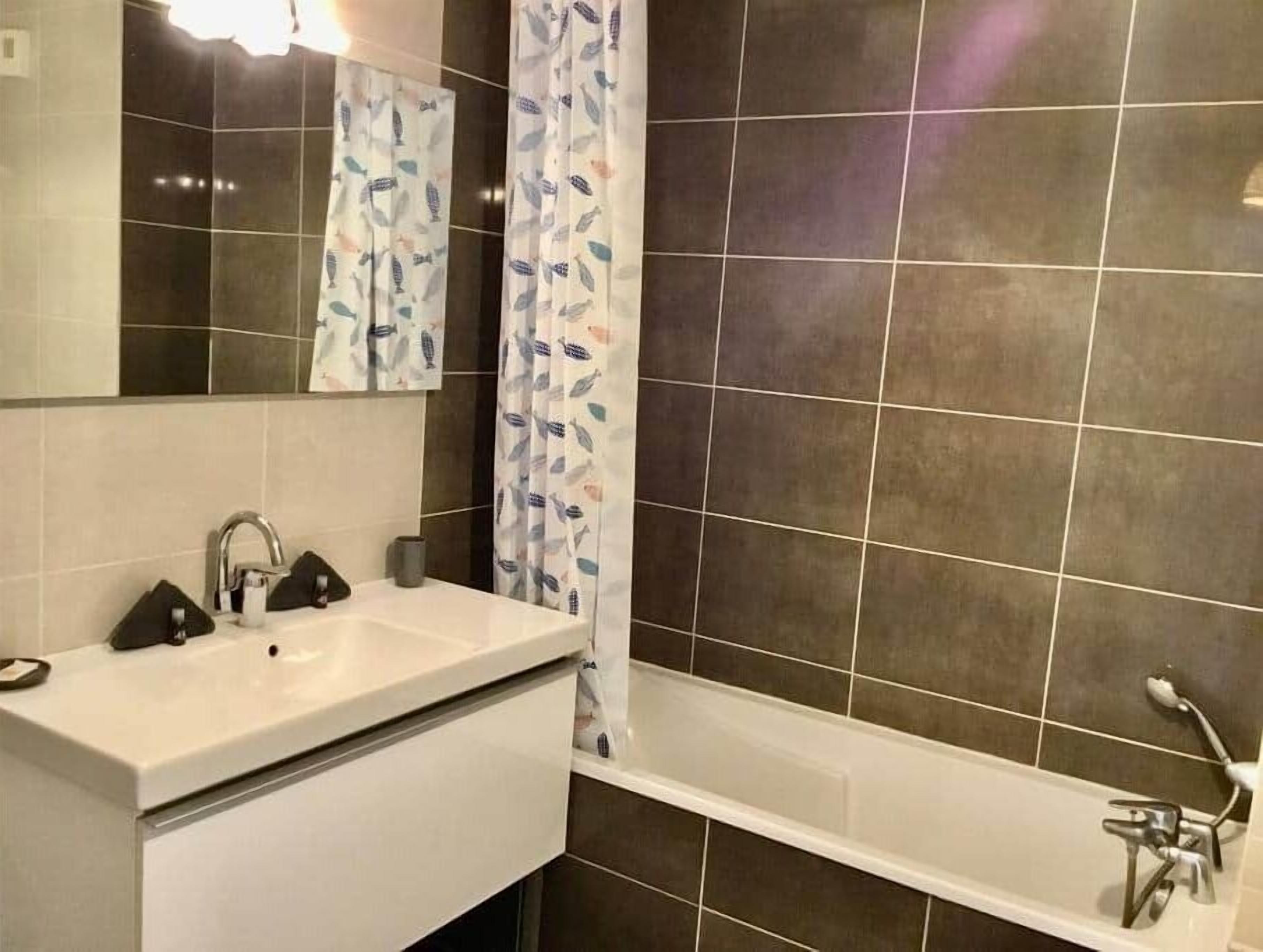 A bathroom with a white sink, a mirror, a shower curtain with a leaf pattern, and a bathtub.