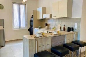 Una cocina compacta con una isla central, taburetes de bar y un ventanal con cortinas.