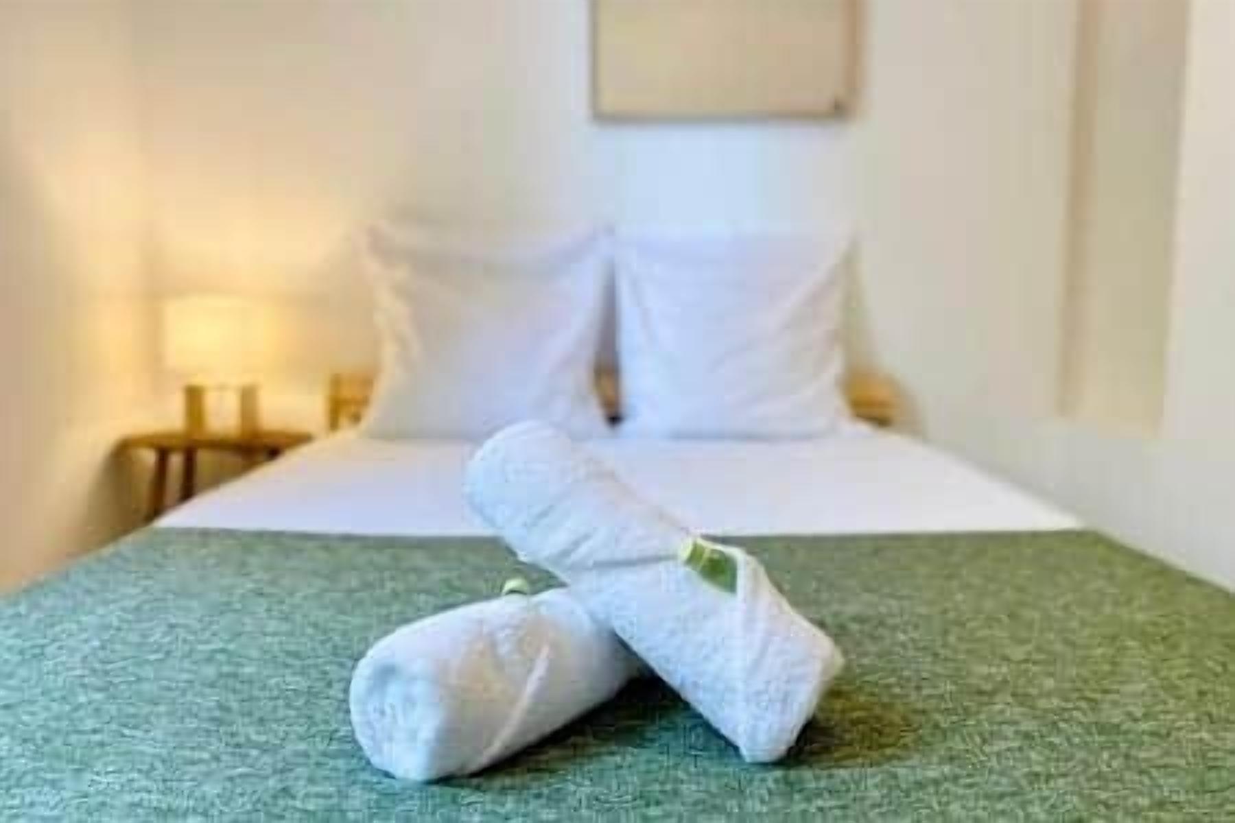 Un llit ben fet amb roba blanca i un llençol verd en una habitació d'hotel.