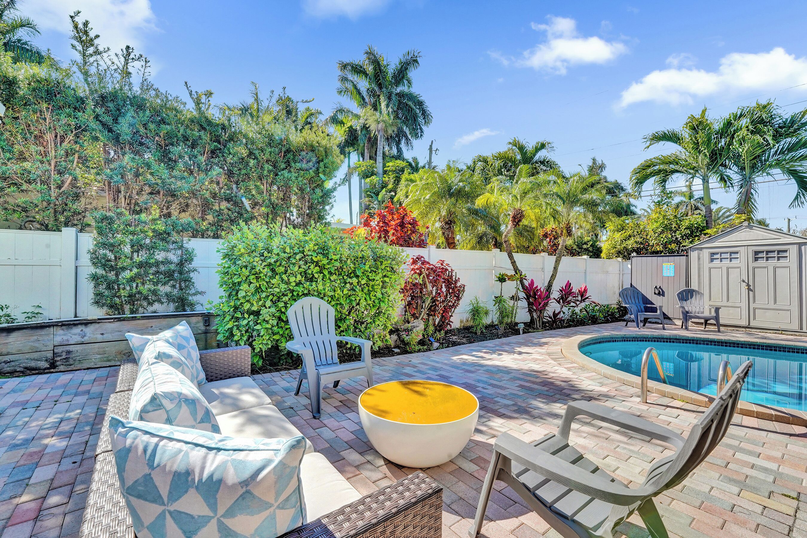 A backyard with a pool, outdoor furniture, and a variety of plants.
