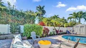 Un patio trasero con piscina, mobiliario exterior y diversas plantas.
