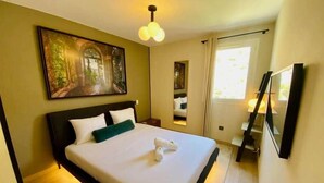 A neatly made bed with white linens and a green pillow, a painting on the wall, and a large window with curtains. - "Le Soleil" Superb T3 with pond view air-conditioning parking pool (Sète)