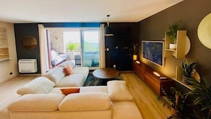 A modern living room with a sectional sofa, a round coffee table, and a large window with a view. - "Le Soleil" Superb T3 with pond view air-conditioning parking pool (Sète)