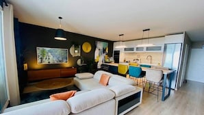 A modern living room with a sectional sofa, a dining area with bar stools, and a kitchen with white cabinets. - "Le Soleil" Superb T3 with pond view air-conditioning parking pool (Sète)
