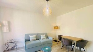 Een moderne woonkamer met een grijze bank, een ronde salontafel, een eettafel met stoelen, een vloerlamp en een hanglamp.