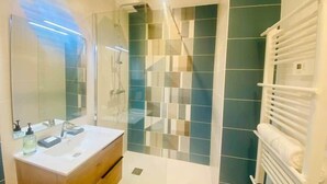 Een moderne badkamer met een douchecabine van glas, een houten wastafelmeubel en een handdoekrek.