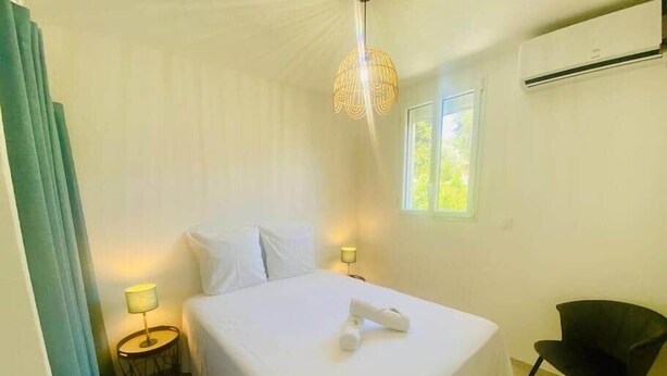 Een slaapkamer met een bed, nachtlampjes, een stoel, een raam en een airconditioning.