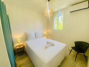 Ein Schlafzimmer mit Bett, Nachttischlampen, einem Sessel, einem Fenster und einer Klimaanlage.