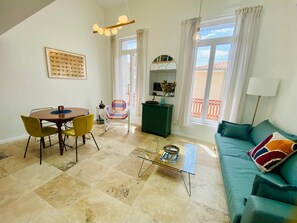 A living room with a round table, chairs, a sofa, a coffee table, a hanging light fixture, a mirror, and a window with curtains. - "Le Refuge Duplex Quartier Haut, air-conditioned (Sète)