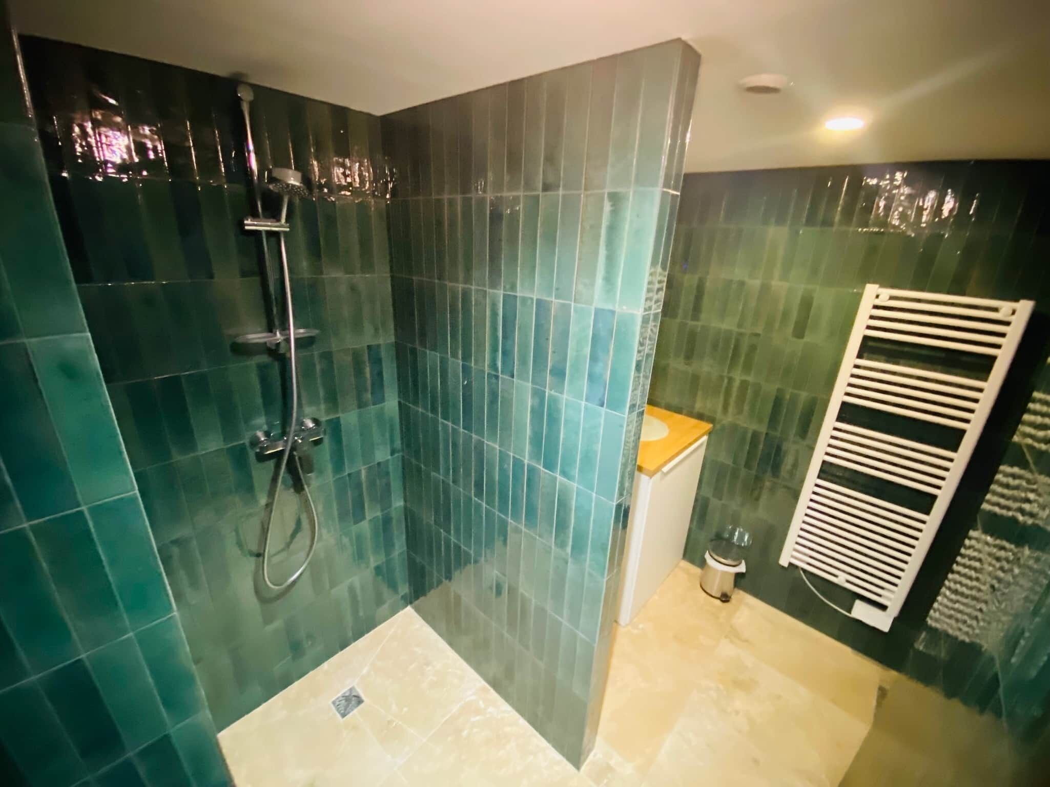 Ducha con azulejos verdes, inodoro blanco y un perchero para toallas.