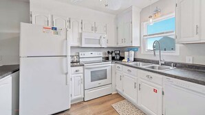 Une cuisine moderne avec des meubles blancs, un réfrigérateur, un four à micro-ondes, un four et un évier.