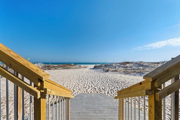 A wooden staircase leading to a sandy beach with a clear sky. - š Beachfront Complex | Community Pool + Covered Parking | Sunrise Village 105 (Gulf Shores)