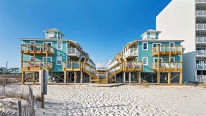 Un hÎtel en bord de mer, avec des bùtiments à deux étages, des balcons en bois et une plage de sable au premier plan.