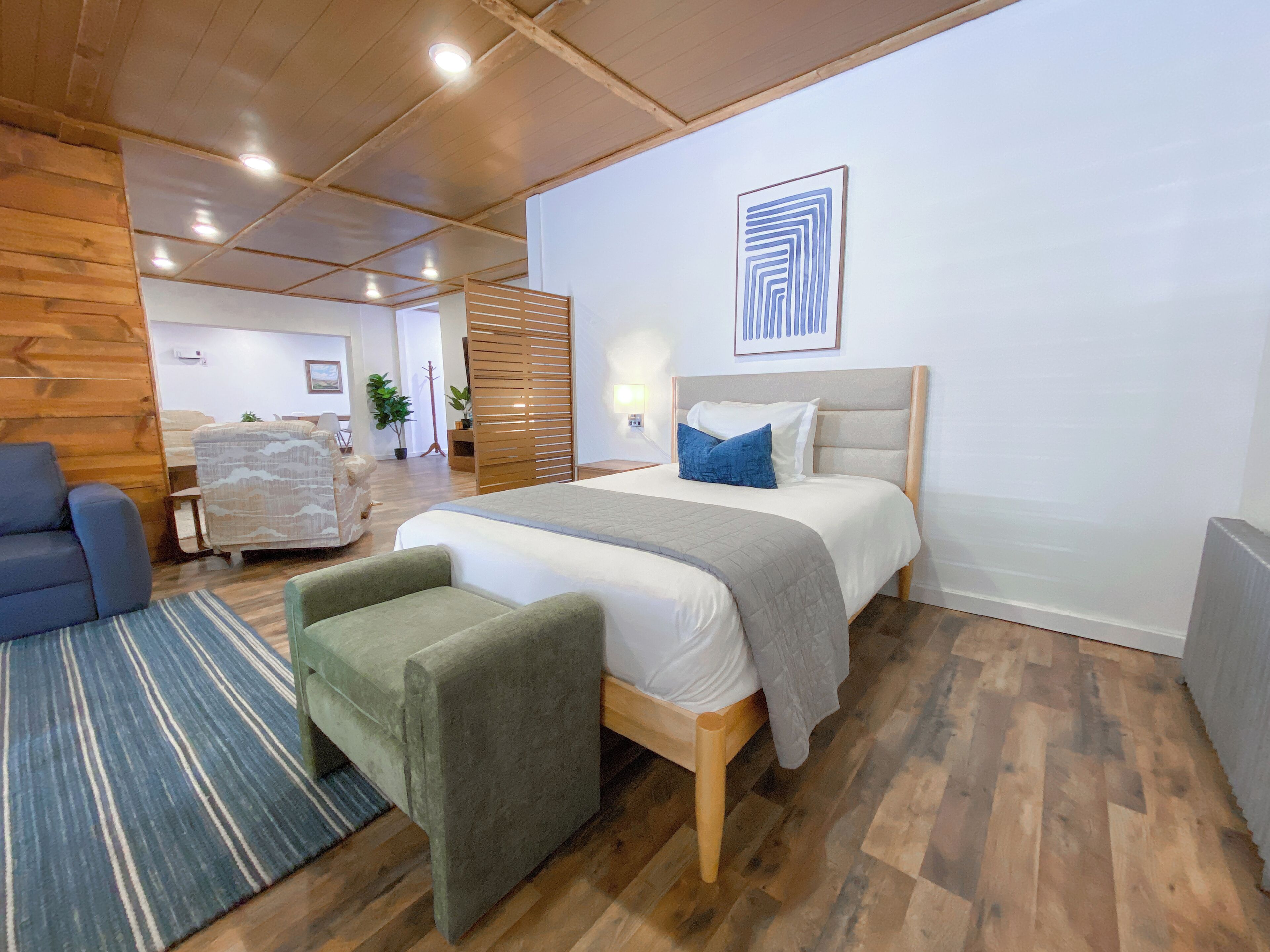 A modern bedroom with a wooden bed, a green armchair, a blue armchair, and a patterned rug.