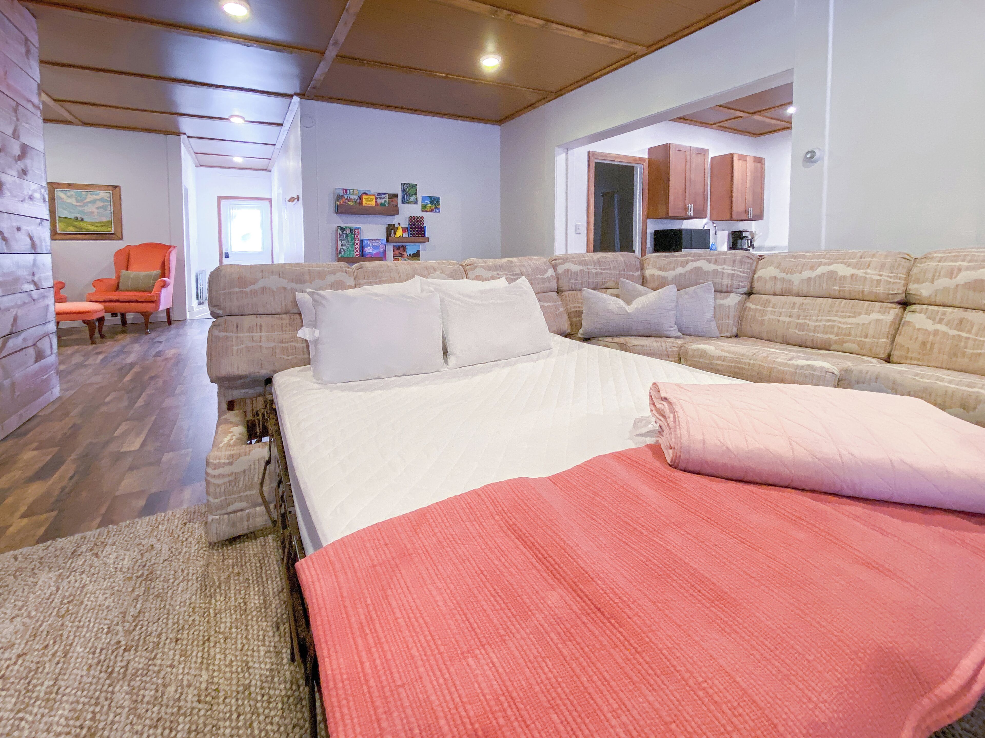 Un dormitorio moderno con una cama grande, un sofá y una silla. Se ve una cocina al fondo.