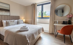 A hotel room with a bed, a desk, a chair, a window with curtains, and a round mirror on the wall. - Tigh Mary Donals Bar & Rooms at Whitegates (Killarney)