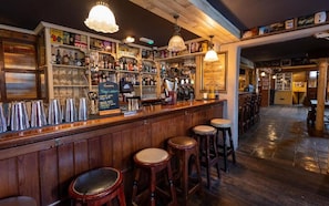 A bar area with wooden bar counters, stools, and a variety of bottles and glasses. - Tigh Mary Donals Bar & Rooms at Whitegates (Killarney)