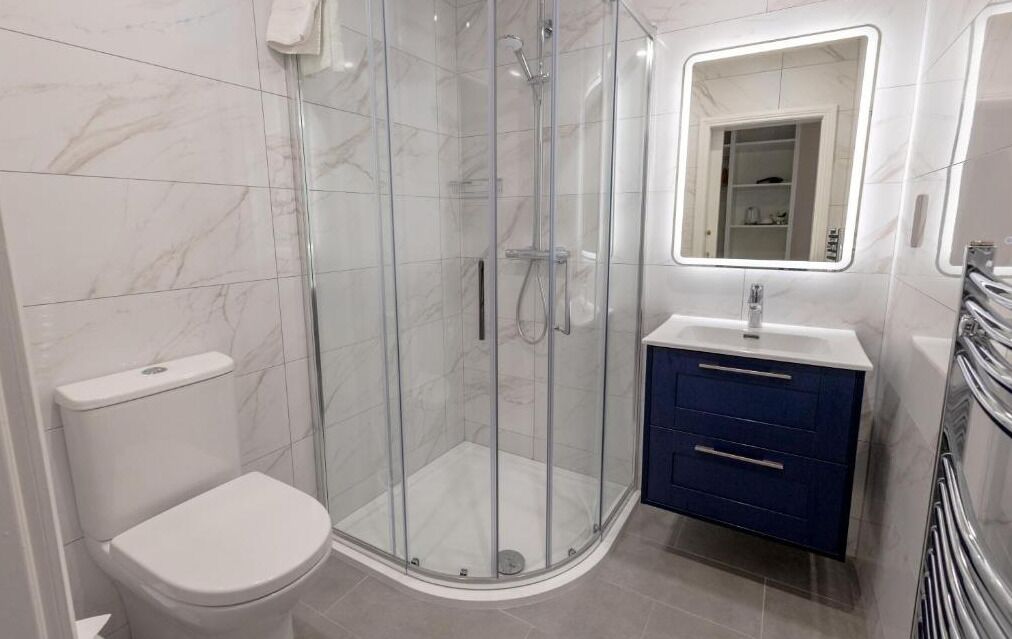 Un baño moderno con ducha acristalada, inodoro blanco y tocador con espejo.