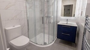 Ein modernes Badezimmer mit einer gläsernen Duschkabine, einer weißen Toilette und einem Waschtisch mit Spiegel.