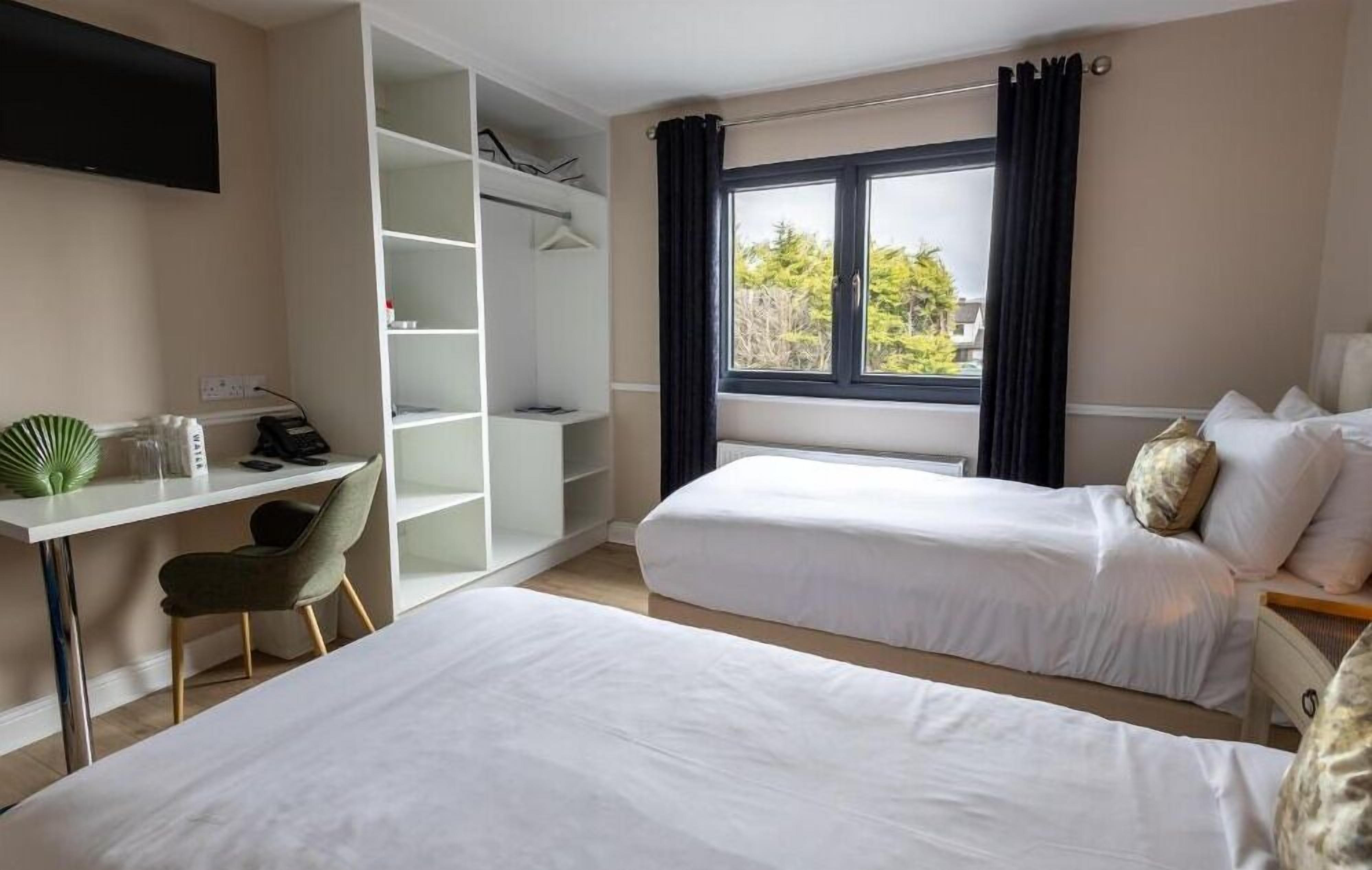 Habitación de hotel con dos camas, un escritorio, una silla, un televisor y una ventana con cortinas.
