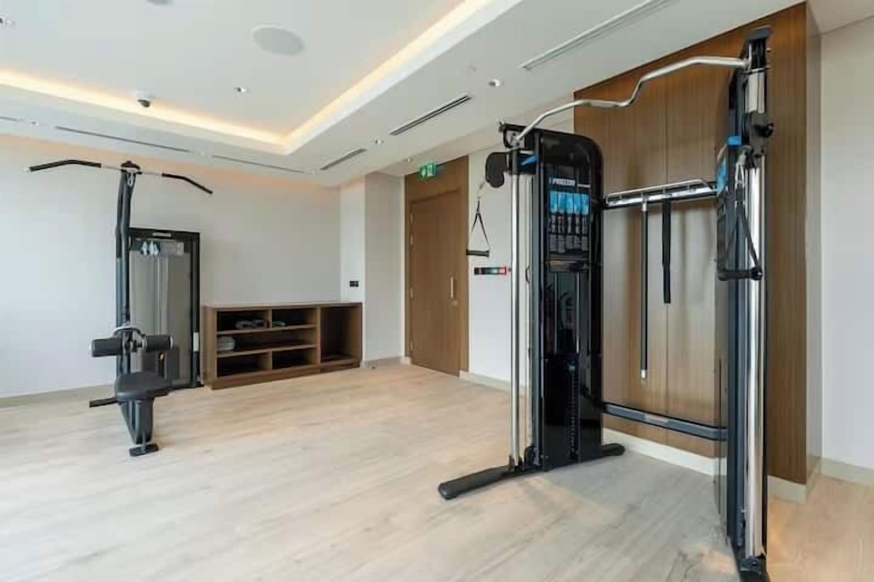 Une salle de remise en forme équipée de matériel d’exercice, dotée d’un plancher en bois et d’une porte donnant sur une autre pièce.