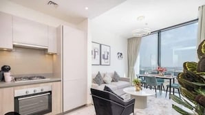 A modern apartment with a kitchen, dining area, and a large window offering a city view. - Vogue | Sobha Hartland close to Downtown Dubai Mall | Burj Khalifa (Dubai)