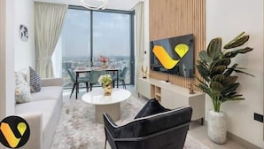 A modern living room with a sofa, a black chair, a round coffee table, and a TV on the wall. - Vogue | Sobha Hartland close to Downtown Dubai Mall | Burj Khalifa (Dubai)