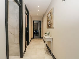 A hallway with a marble floor, a white console table with a vase of flowers, and a painting on the wall.